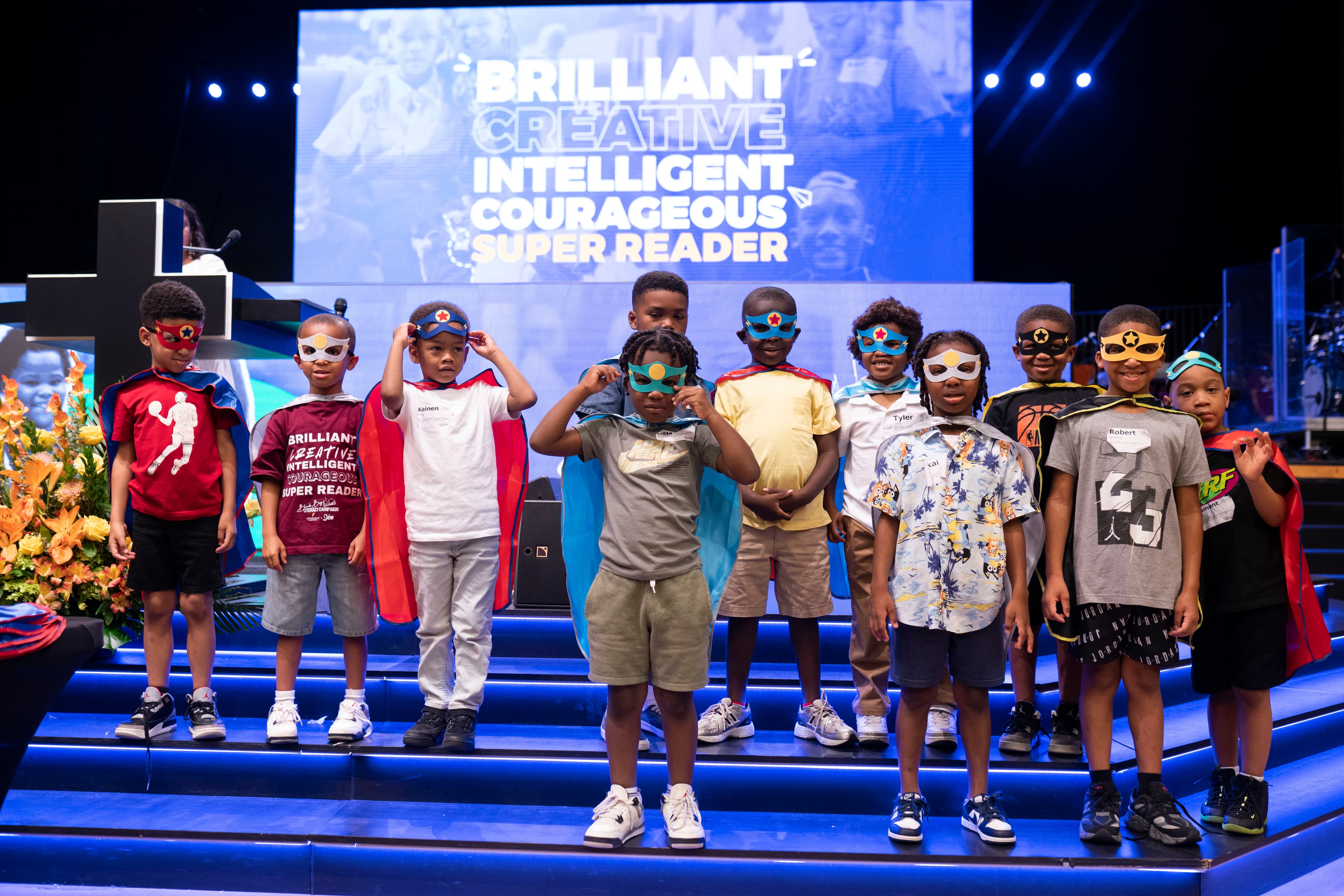 Boys in capes and masks on stage at the Cape Ceremony