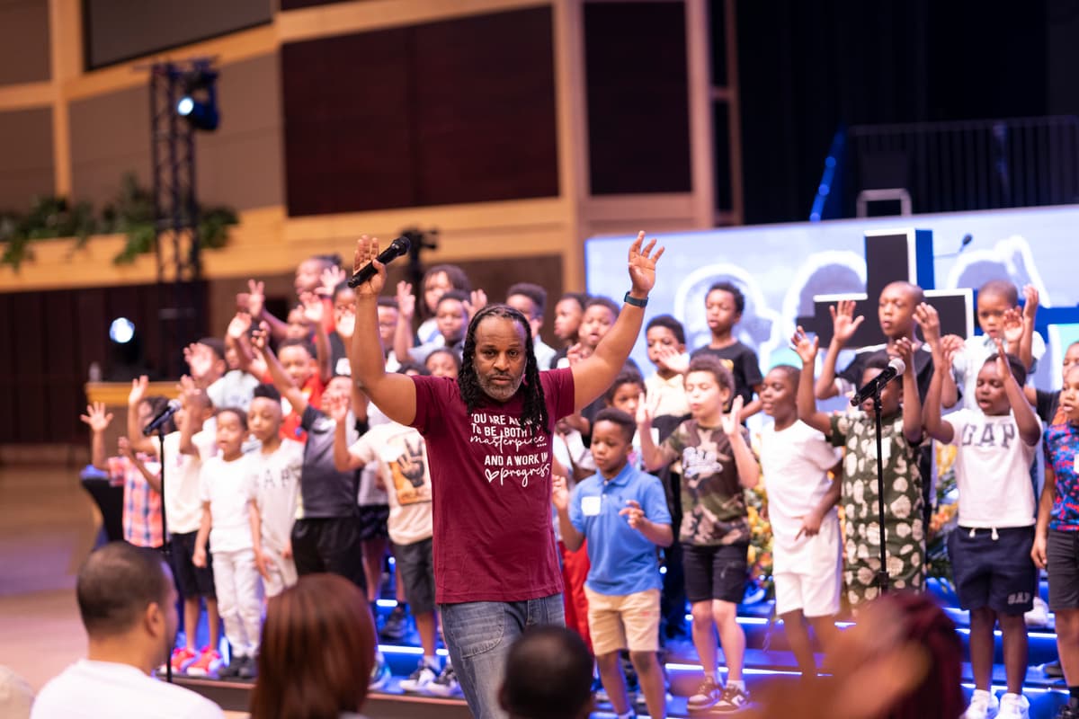 Leader with arms raised, boys worshipping together with cross